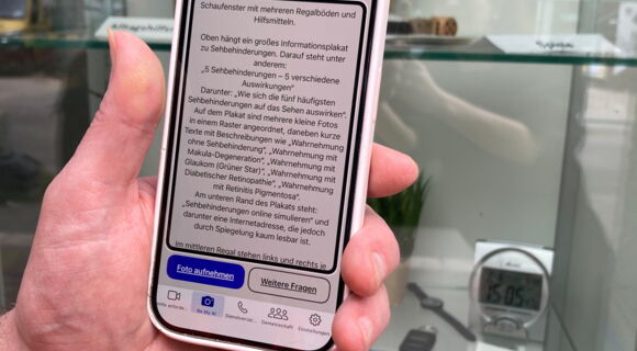 Eine linke Hand richtet ein Smartphone auf ein Schaufenster. Auf dem Display ist viel Text zu erkennen