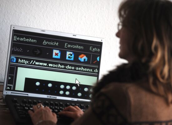 Eine Frau sitzt an einem Computer und scrollt durch eine Webseite. Ihre Darstellung ist invertiert.