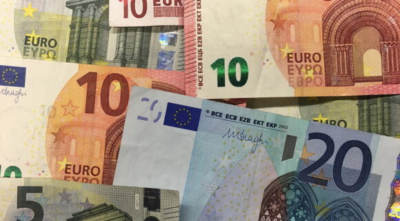 Mehrere Euro-Banknoten in verschiedenen Werten (5, 10, 20) liegen überlappend aufeinander. Die Scheine zeigen unterschiedliche Farben und Architektur-Motive, die typisch für Euro-Noten sind.