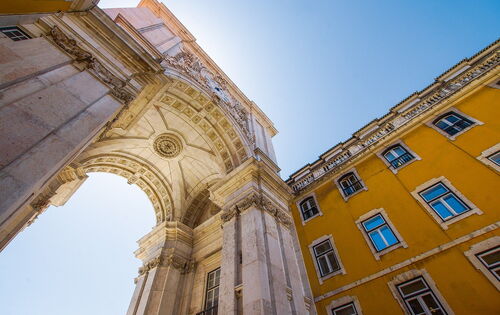 Ein Stadtbild von Lissabon. Ein hoher Torbogen erhebt sich über die Kamera.