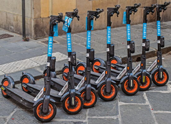 Sieben E-Roller stehen in Reih und Glied am Straßenrand. Im Hintergrund ist ein Orientierungsfeld zu sehen.