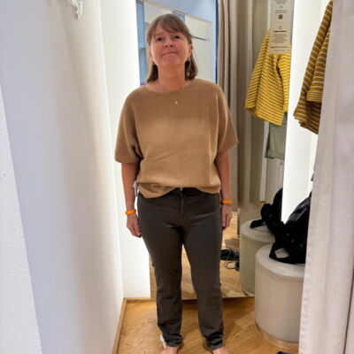Tamara Ströter steht in einem kurzärmeligen beigen Pullover und in Jeans in einer Umkleidekabine. Sie hat längeres glattes Haar.