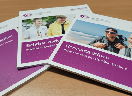 Drei Ausgaben der DBSV-Jahrespublikation "Weitersehen" liegen aufgefächert auf einem Tisch. "Leben mit Sehverlust", "Sichtbar stark" und "Horizonte öffnen" steht weiß auf purpur auf dem jeweiligen Heft.
