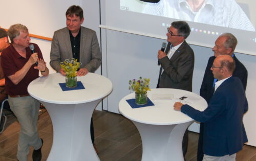 Oded Heilbronner, Andreas Bethke und Hans Neugebauer stehen bei der Gesprächsrunde an weißen Tischen. Prof. Heilbronner hält ein Mikrofon.