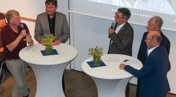 Oded Heilbronner, Andreas Bethke und Hans Neugebauer stehen bei der Gesprächsrunde an weißen Tischen. Prof. Heilbronner hält ein Mikrofon.