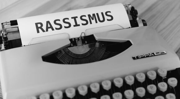 Eine Schreibmaschine mit einem angefangenen Blatt. In Großbuchstaben steht Rassismus dort geschrieben.