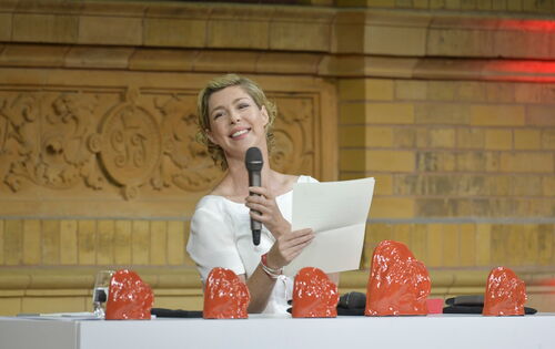 Die Schauspielerin Brigitte Zeh hält eine Laudatio beim Deutschen Hörfilmpreis 2023.  Sie steht hinter einem Pult, auf dem die Trophäen, die „ADeles“, aufgereiht stehen