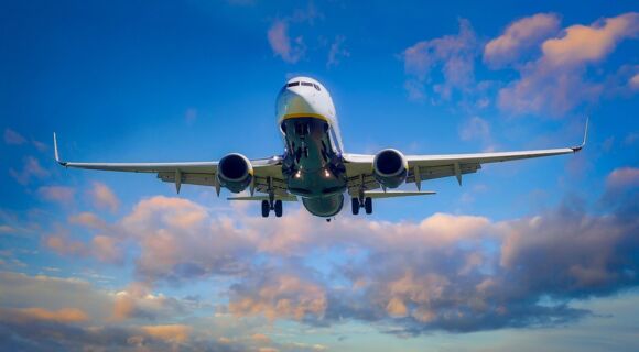 Ein Flugzeug in der Luft, von schräg unten fotografiert. Der Himmel ist blau, die Wolken golden angestrahlt.