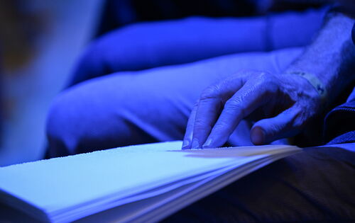 Praktisch und kreativ: eine Hand fährt beim blauen Licht eines Konzerts über ein Liederbuch in Braille-Schrift.