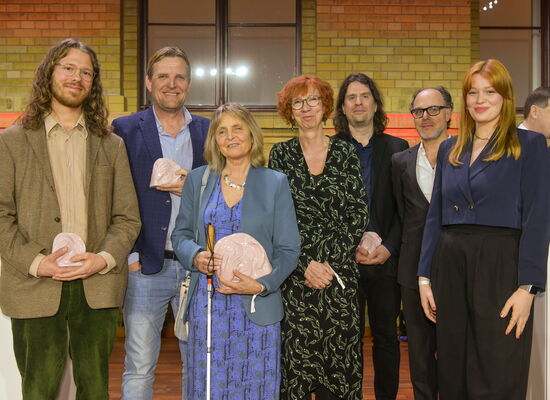 In festlicher Kleidung steht das AD-Team des Animationsfilms „Wo ist Anne Frank“  auf der Bühne. Es gewann die ADele in der Kategorie „Kinder- und Jugendfilm“.  Einige Team-Mtglieder halten die Keramik-Trophäe in den Händen.