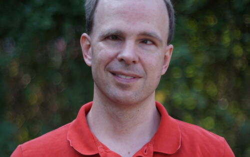 Alexander Pfingstl lächelt in die Kamera. Er hat kurzes, an den Seiten dichteres Haar und trägt ein Shirt mit kurzem Kragen.