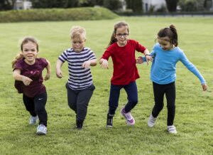 Vier Kinder, zum Teil mit Behinderung, rennen Hand in Hand über eine Wiese. Sie tragen bunte T-Shirts und haben Spaß.