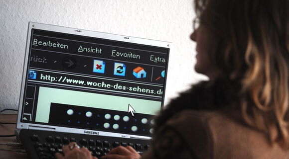 Eine Frau sitzt an einem Computer und scrollt durch eine Webseite. Ihre Darstellung ist invertiert.