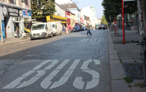 Eine Hamburger Bushaltestelle. Auf der freien Fahrbahn ist mit den weißen Worten "BUS" die Haltezone für den ÖPNV markiert.