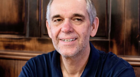 Kopf-Schulter-Portrait von Ottmar Miles-Paul: Er lächelt in die Kamera. Sein Haar ist grau, er hat eine hohe Stirn und dunkle Augenbrauen.