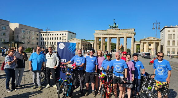 Die Radfahrer posieren zusammen mit Sportler Thomas Ulbricht und den Vertreterinnen der französischen Botschaft vor dem Brandenburger Tor. Sie tragen passende blaue und violette T-Shirts. Ihre Räder sind mit Blumen geschmückt.