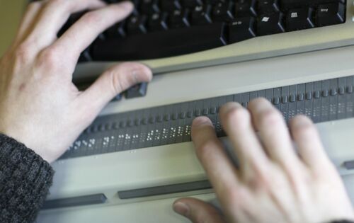 Ein Paar Hände liest auf einer Braillezeile an einem Laptop.