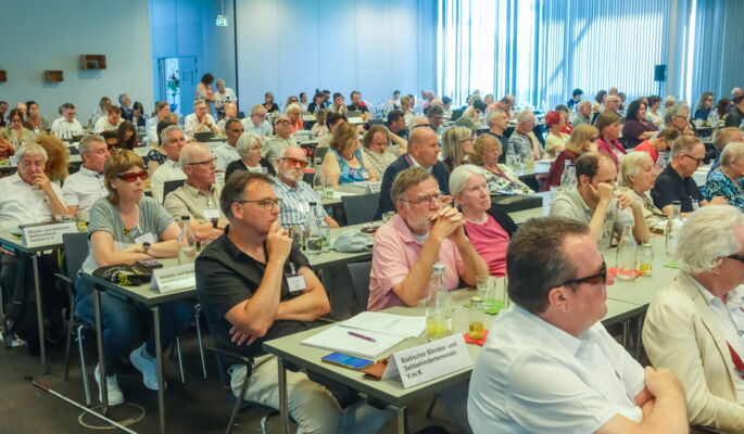 An langen Tischreihen sitzen die Delegierten des Verbandstags, ein gemischtes Publikum.