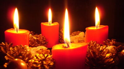 Vier rote Kerzen brennen auf einem Adventskranz. Er ist mit Tannenzapfen verziert. Die Kerzen schaffen ein warmes Licht.