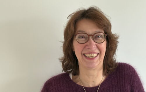 Anne Niesen lacht in die Kamera. Sie hat mittellange, wellige, dunklere Haare und trägt eine Brille mit dunklem Rahmen.