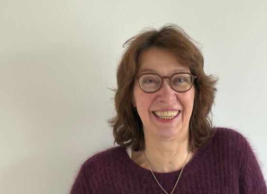 Anne Niesen lacht in die Kamera. Sie hat mittellange, wellige, dunklere Haare und trägt eine Brille mit dunklem Rahmen.