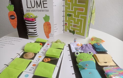 Interaktives Tastbuch „Lume der Karottenfresser“ mit Stofffiguren, Taschen, Labyrinth und verschiedenen taktilen Spielelementen auf mehreren geöffneten Buchseiten.