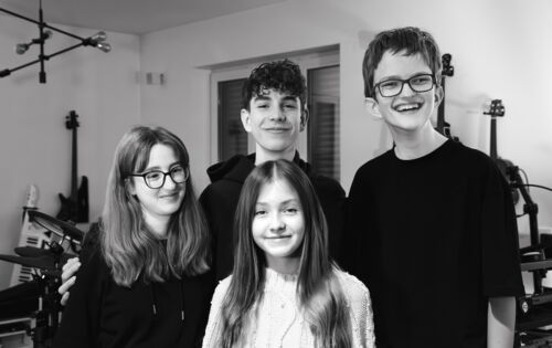 Die Band Rockytrio, vier Jugendliche zwischen 13 und 16, stehen in einem Musikraum vor Instrumenten und schauen freundlich lächelnd in die Kamera.