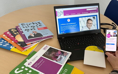 Auf einem Tisch steht ein Laptop, das eine Seite von Sichtweisen-online zeigt. Daneben ein Stapel Sichtweisen-Hefte, die Publikation „Weitersehen 2024“ und eine Daisy-CD.