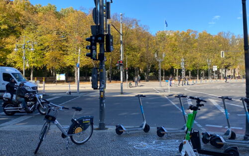 Auf einem Gehweg stehen kreuz und quer verschiedenfarbige E-Roller.