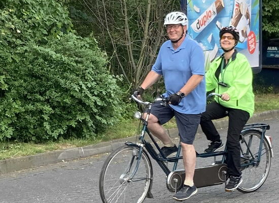 Petra Bognitz und ihr Pilot Volker Weinlich fahren auf einem Tandem eine Straße entlang. Beide tragen einen Helm.