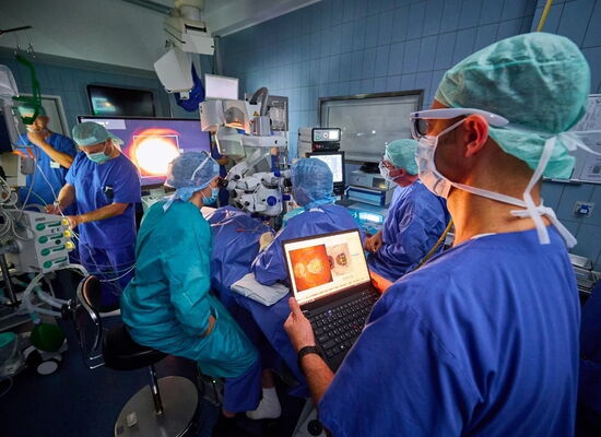 Implantation - eines elektronischen Netzhaut-Chips in der Augenklinik des UKB durch Prof. Frank Holz. Mehrere Ärzte nehmen die OP vor und verfolgen sie über Bildschirme.