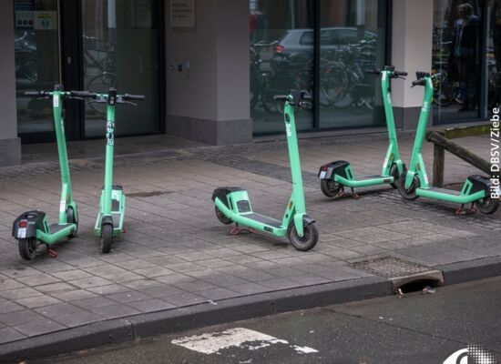 Fünf grüne E-Roller stehen kreuz und quer auf dem Gehweg.