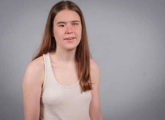 Porträt von Vreni Bock. Ihre langen, braunen Haare trägt sie offen, dazu ein schlichtes, weißes Kleid ohne Ärmel.