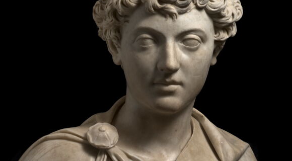 Büste von Marcus Aurelius, die den jungen Mann mit lockigen Haaren und vollen Lippen zeigt. An seiner Schulter befästigt eine runde Brosche seinen Umhang.