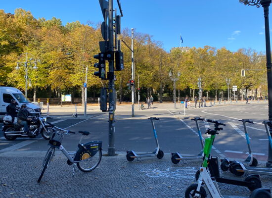 Auf einem Gehweg stehen kreuz und quer verschiedenfarbige E-Roller.