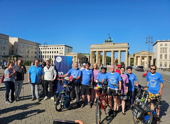 Die Radfahrer posieren zusammen mit Sportler Thomas Ulbricht und den Vertreterinnen der französischen Botschaft vor dem Brandenburger Tor. Sie tragen passende blaue und violette T-Shirts. Ihre Räder sind mit Blumen geschmückt.