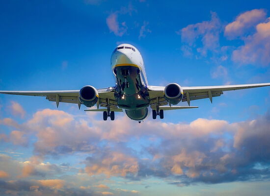 Ein Flugzeug in der Luft, von schräg unten fotografiert. Der Himmel ist blau, die Wolken golden angestrahlt.