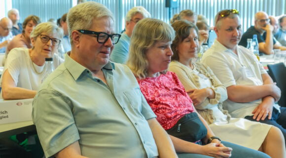 Prof. Thomas Kahlisch und Andrea Katemann sitzen nebeneinander im Plenum. Um sie herum andere Teilnehmende des DBSV-Verbandstags. Ihre Aufmerksamkeit ist auf den vorderen Teil des Seminarraums gerichtet.