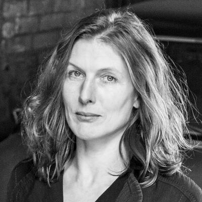 Anja Ellenberger blickt frontal in die Kamera. Sie hat schulterlanges, leicht gewelltes Haar und trägt dunkle Kleidung.