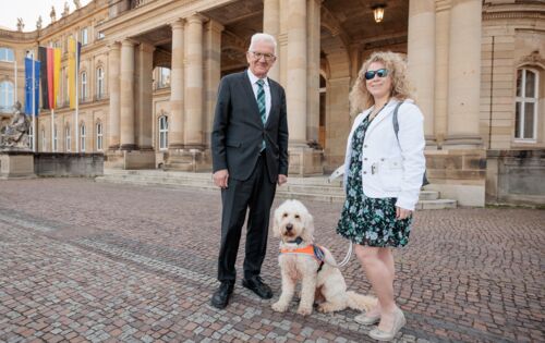 Vor dem Neuen Schloss in Stuttgart stehen von links nach rechts Ministerpräsident Winfried Kretschmann, Festivalführhund Harry und Sichtweisen-Redakteurin Lisa Mümmler.