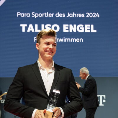 Taliso Engel, Gewinner des Titels Para-Sportler des Jahres 2024, posiert mit seiner Auszeichnung auf der Bühne und zeigt ein stolzes Lächeln.
