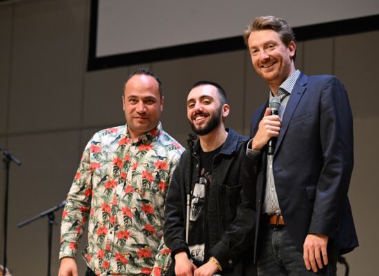 Die drei Comedians Khalil Khalil, Timur Turga und Jochen Prang stehen nebeneinander auf einer Bühne und lachen in die Kamera.