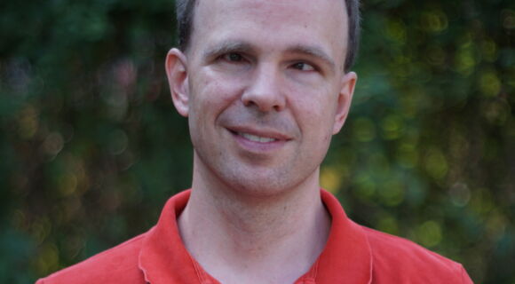 Alexander Pfingstl lächelt in die Kamera. Er hat kurzes, an den Seiten dichteres Haar und trägt ein Shirt mit kurzem Kragen.