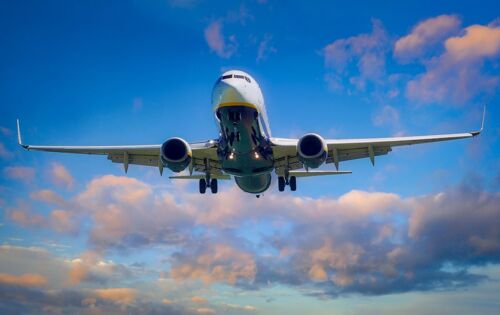 Ein Flugzeug in der Luft, von schräg unten fotografiert. Der Himmel ist blau, die Wolken golden angestrahlt.