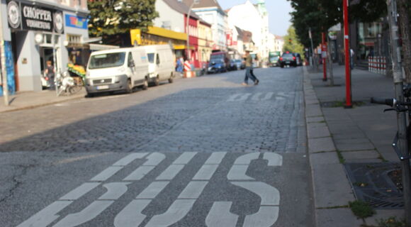 Eine Hamburger Bushaltestelle. Auf der freien Fahrbahn ist mit den weißen Worten "BUS" die Haltezone für den ÖPNV markiert.