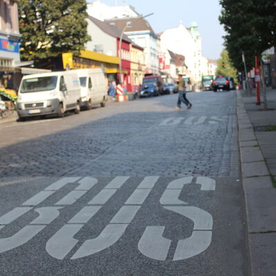 Eine Hamburger Bushaltestelle. Auf der freien Fahrbahn ist mit den weißen Worten "BUS" die Haltezone für den ÖPNV markiert.