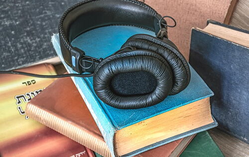 Ein schwarzer Kopfhörer mit gepolsterten Ohrmuscheln liegt auf einem Stapel Bücher. Auch daneben stehen Bücher.