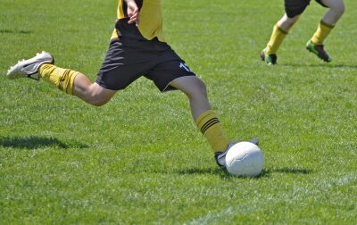 Jemand schießt schwungvoll einen weißen Fußball. Das Trikot ist gelb und schwarz.