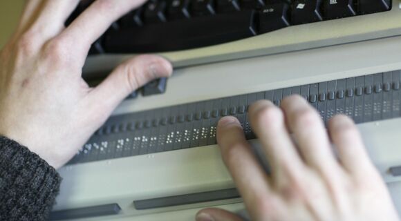 Ein Paar Hände liest auf einer Braillezeile an einem Laptop.