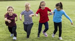 Vier Kinder, zum Teil mit Behinderung, rennen Hand in Hand über eine Wiese. Sie tragen bunte T-Shirts und haben Spaß.
